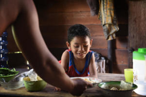 Moses happily receives rice and veggies made by his dad after a day at school. Through fysiotherapy he can now use his hand independently to eat.