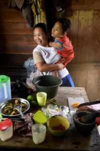 Moses and his mum in the kitchen, just home after school. She carries him inside from the motorbike so he can be in the kitchen amongst family.
